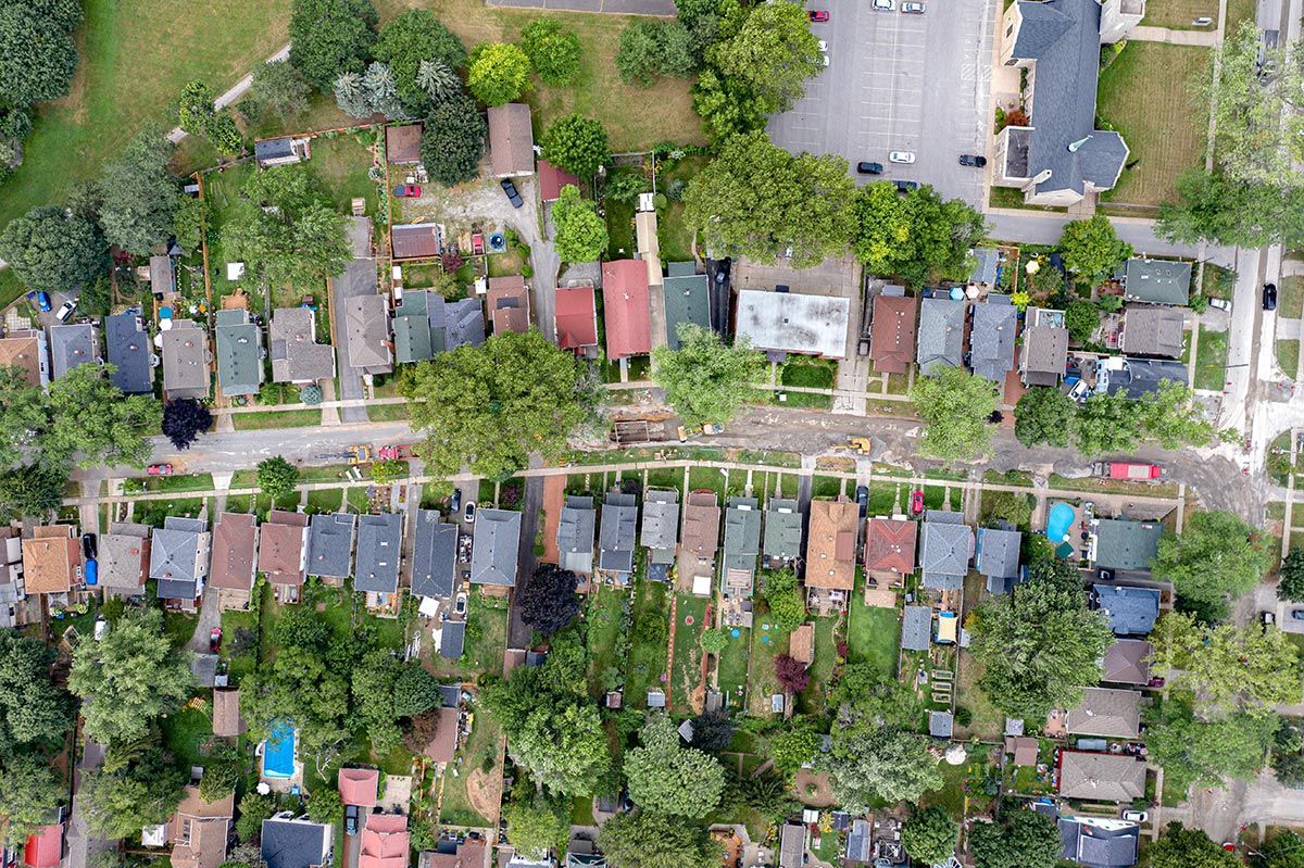 Aerial view of houses with gardens and trees, street in middle.