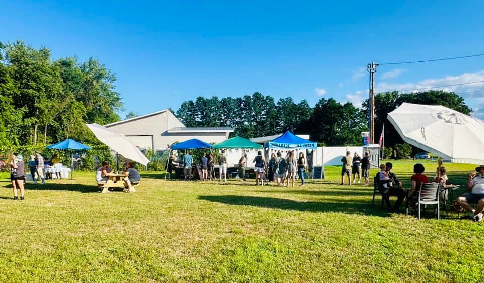 People gather at an outdoor event under tents, sunny day.
