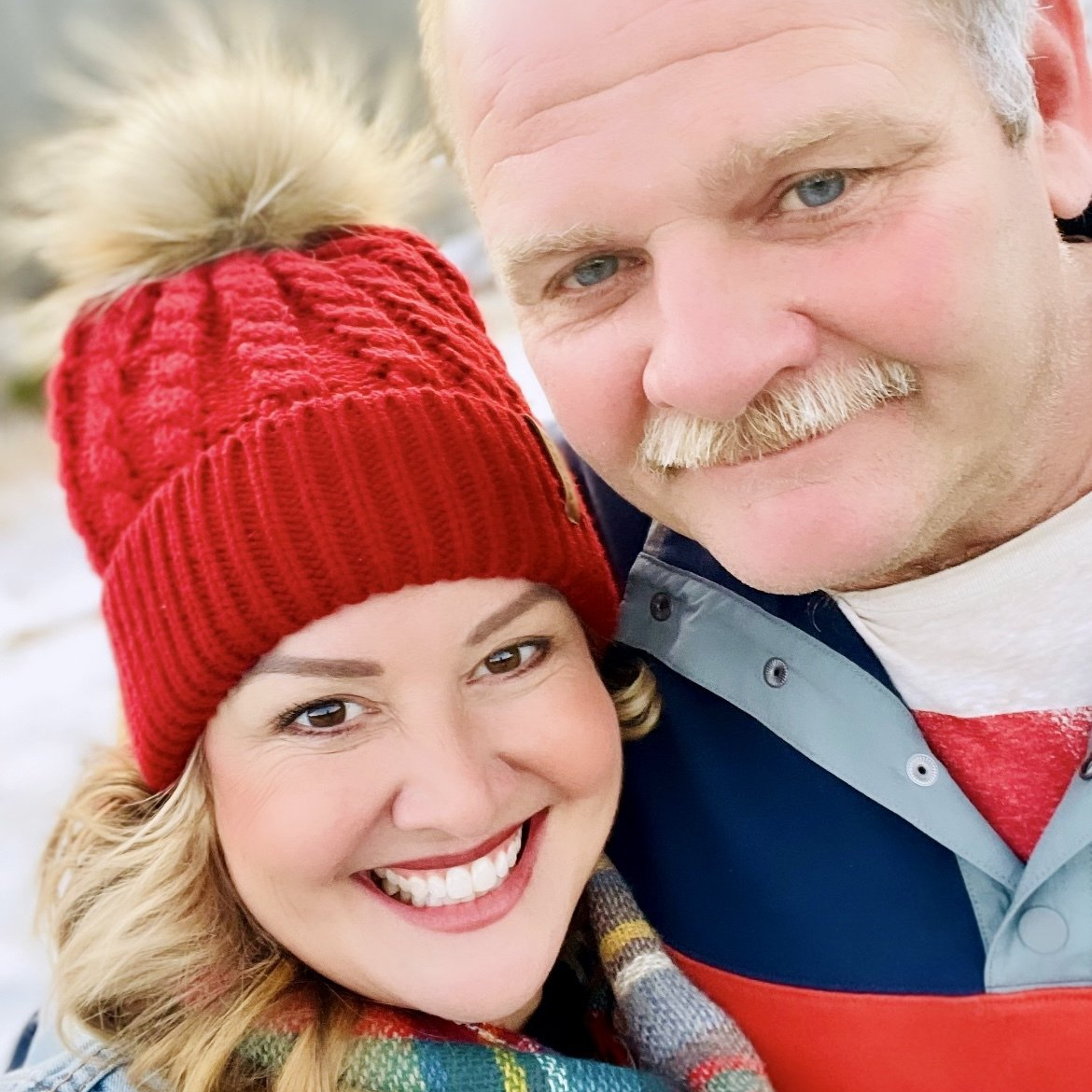 Woman in red hat smiles with man, snowy outdoor background.
