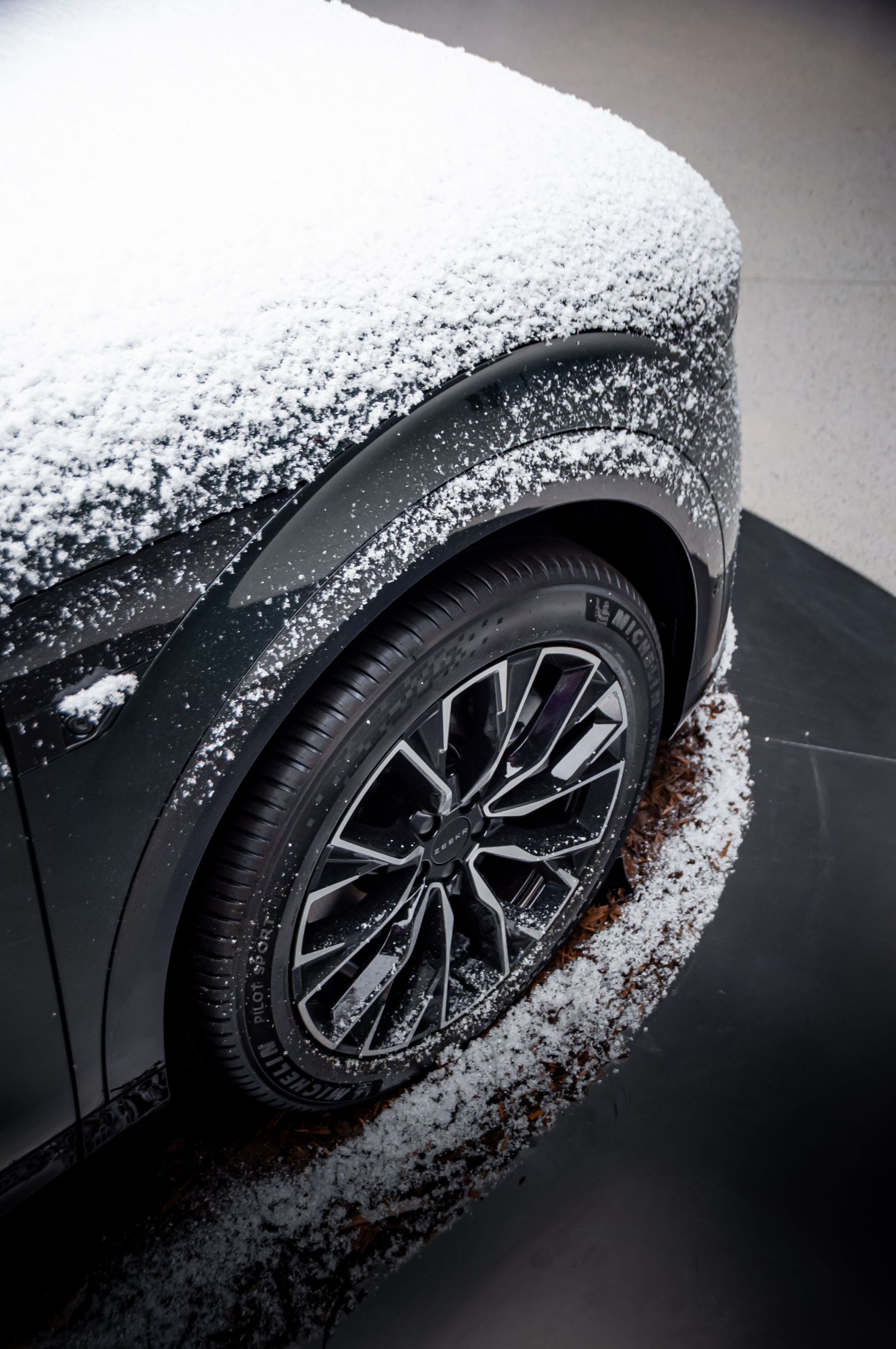 Snow-covered black car wheel and fender parked on a wet road