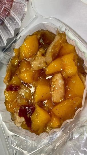 A close up of a peach cobbler in a plastic container.