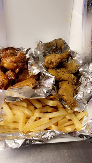 A box of chicken wings and french fries wrapped in tin foil.