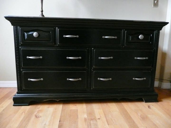Black wooden dresser with six drawers on a hardwood floor against a light wall.