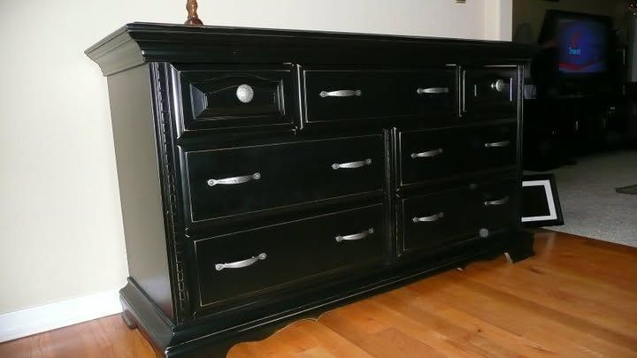 Black dresser with drawers and silver handles against a wall on a hardwood floor