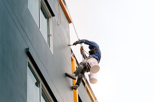 Worker suspended on ropes painting a tall building exterior