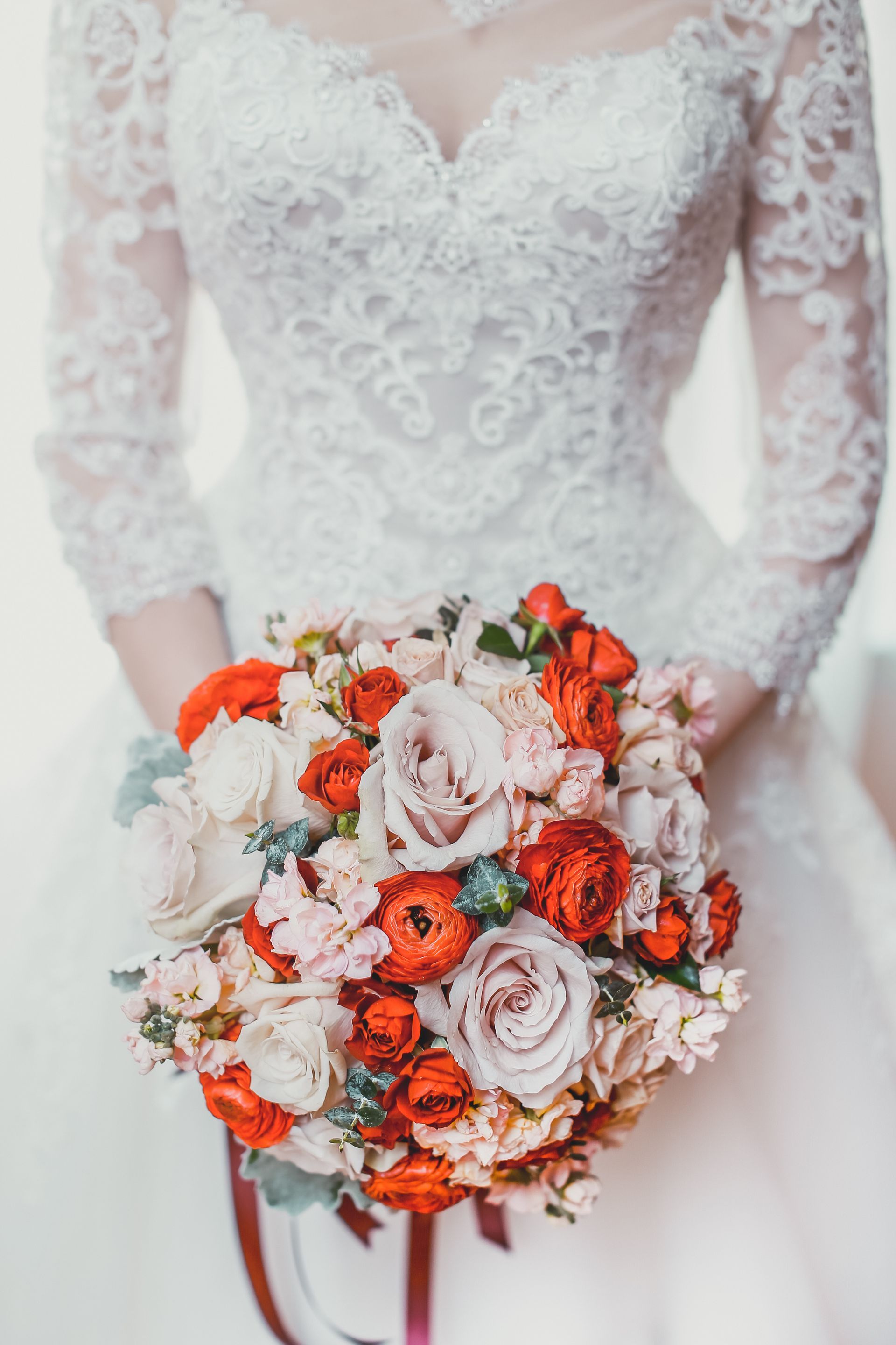 Bride in a lace dress holding a colorful bouquet of roses and other flowers.