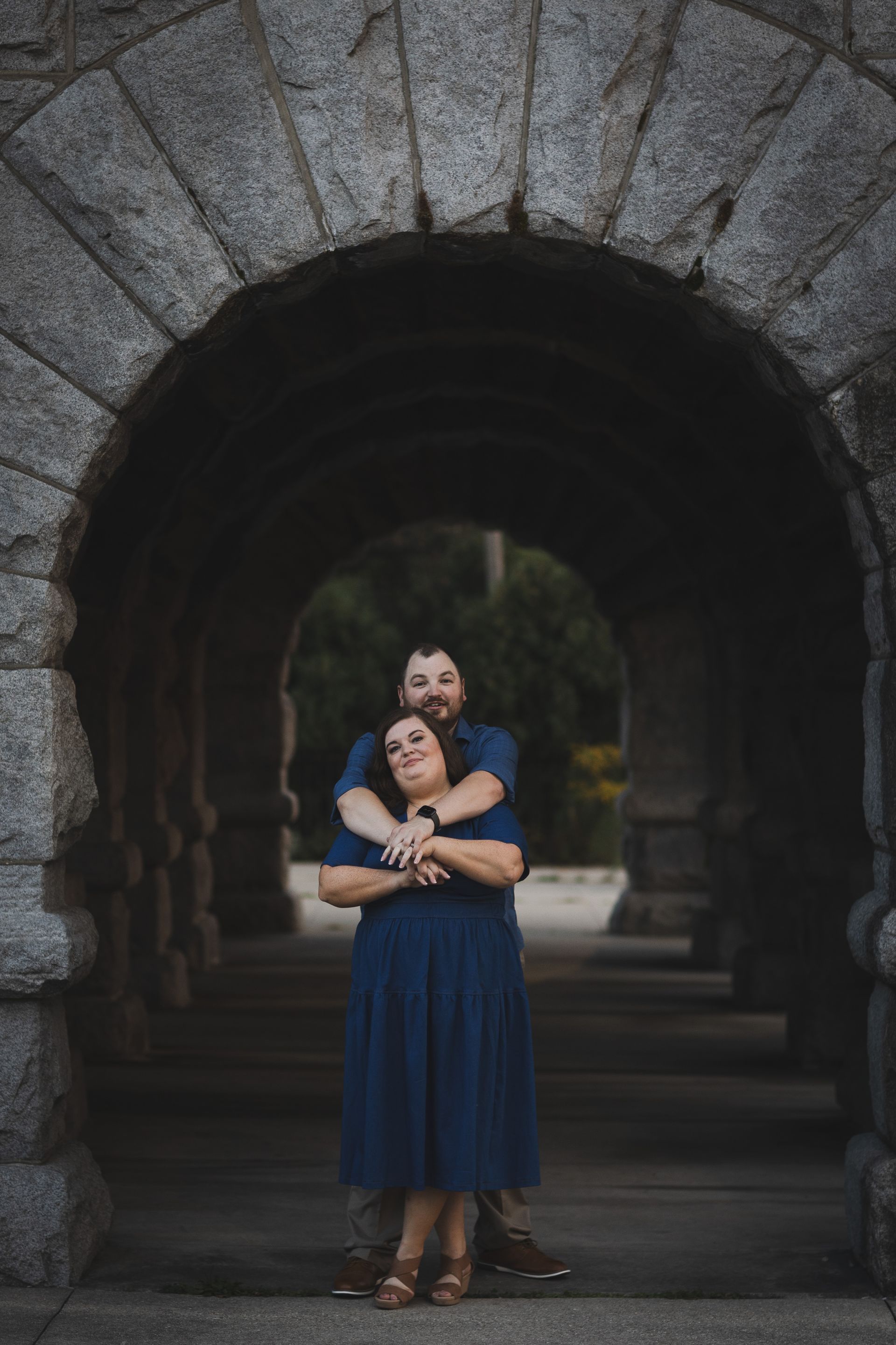 Couple embraces under a stone archway. The woman wears a blue dress, the man a blue shirt.