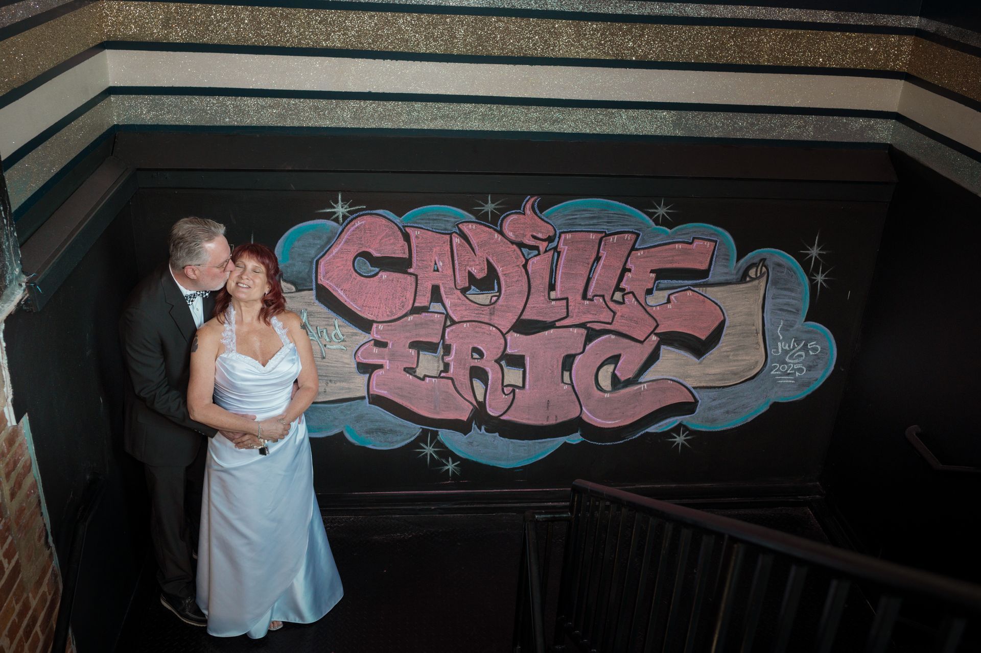Couple kissing by graffiti that reads 