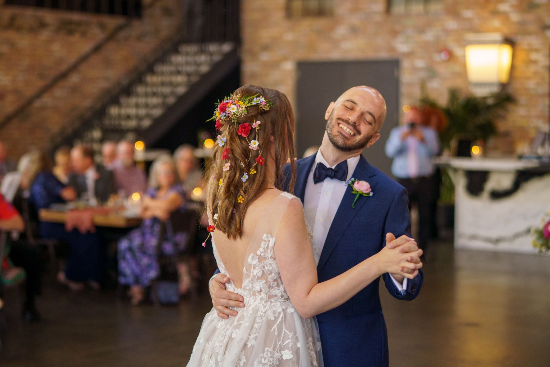 Bride and groom dancing at wedding reception; the groom smiles with the bride's back to the camera.