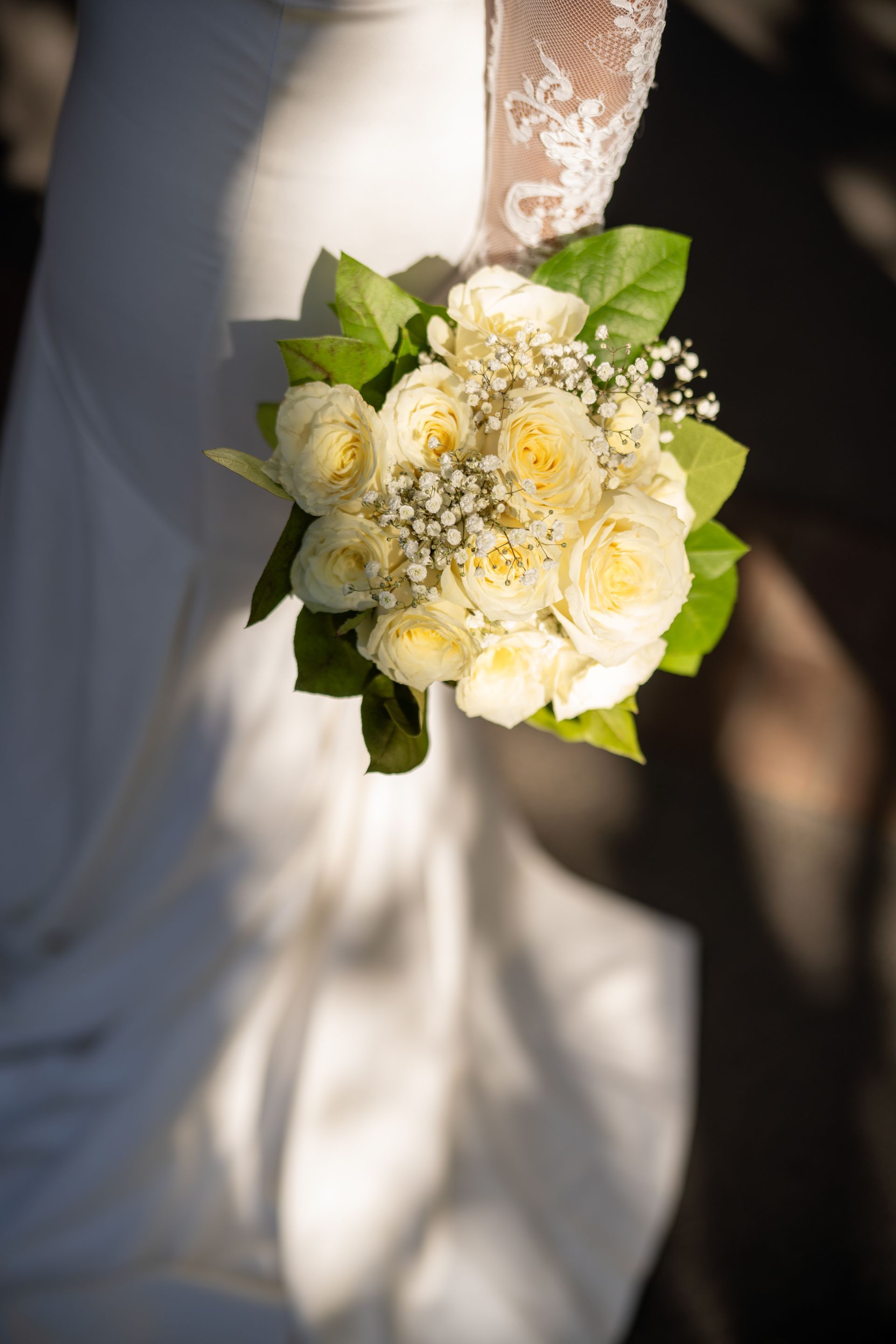 Bride holding a bouquet of cream-colored roses, baby's breath, and green leaves.