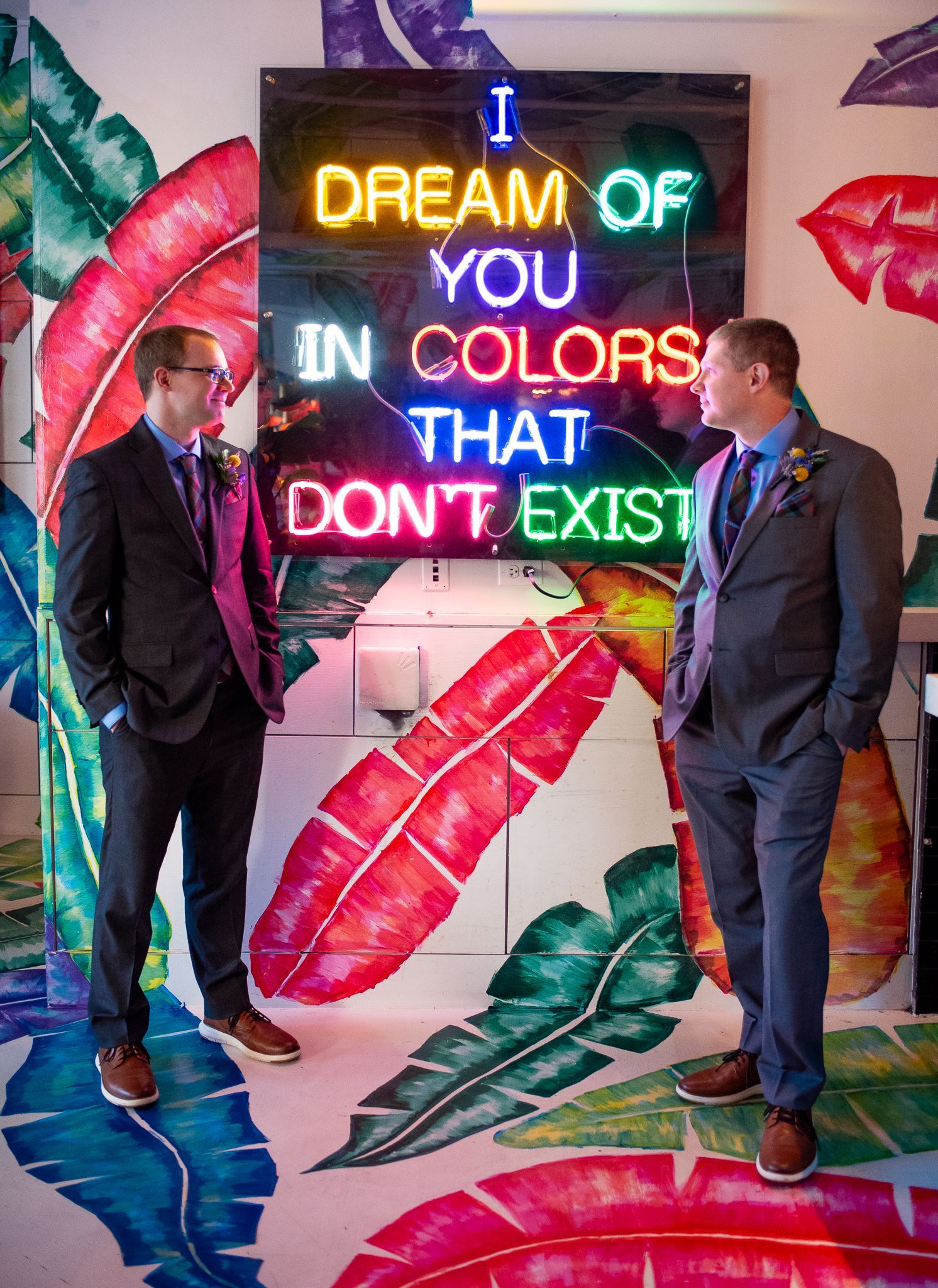 Two men in suits stand near a neon sign that reads 