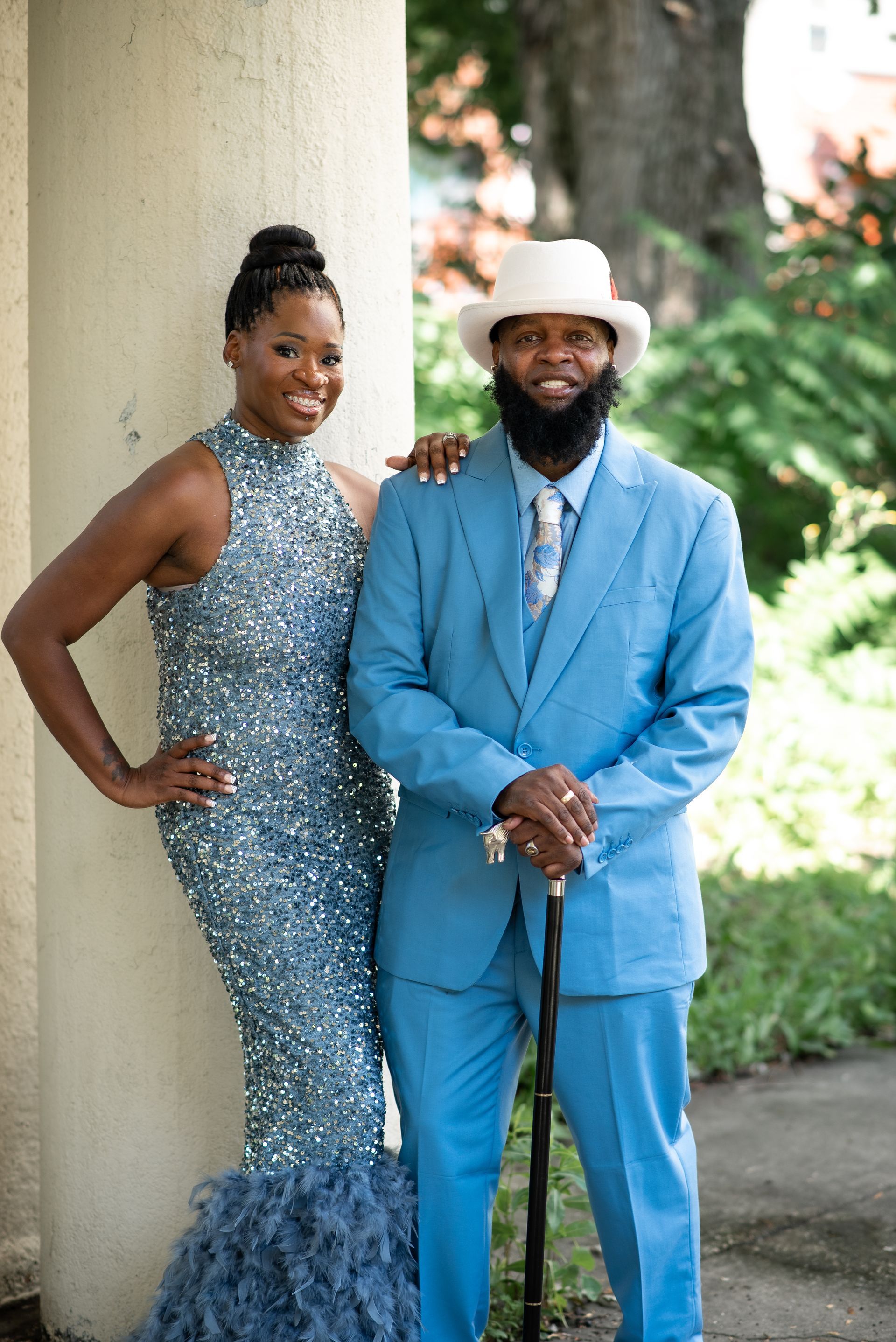 Woman in sequined gown and man in blue suit pose outdoors.