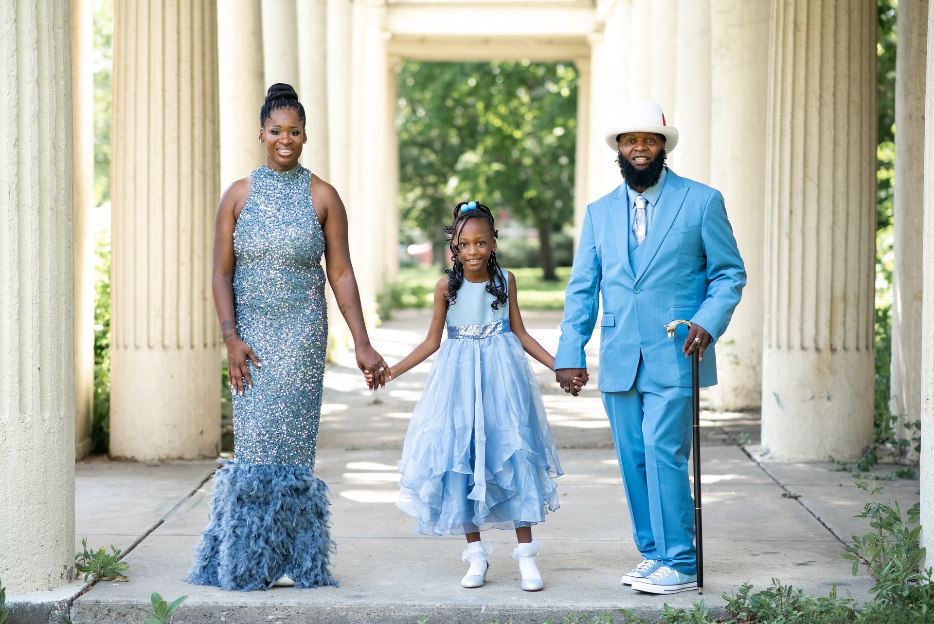 Family, elegantly dressed in blue, holds hands in a columned outdoor setting.