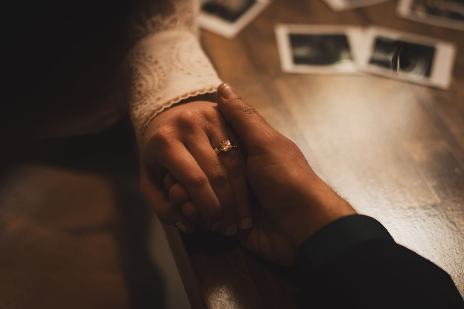 Hands clasped, a ring on a finger, with old photos on a wooden surface.