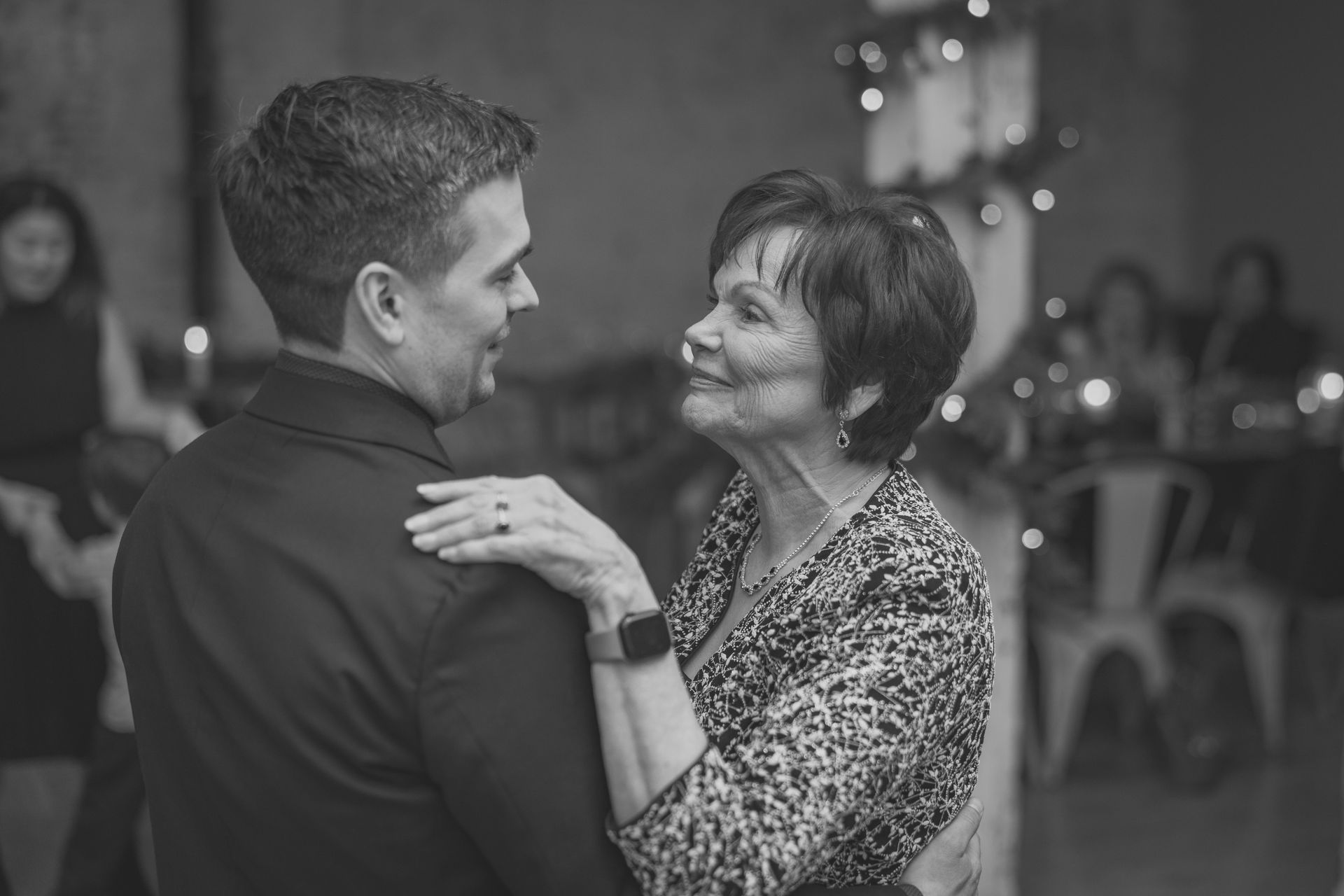 Man and woman dancing, smiling at each other. Indoors, festive setting with blurred background.