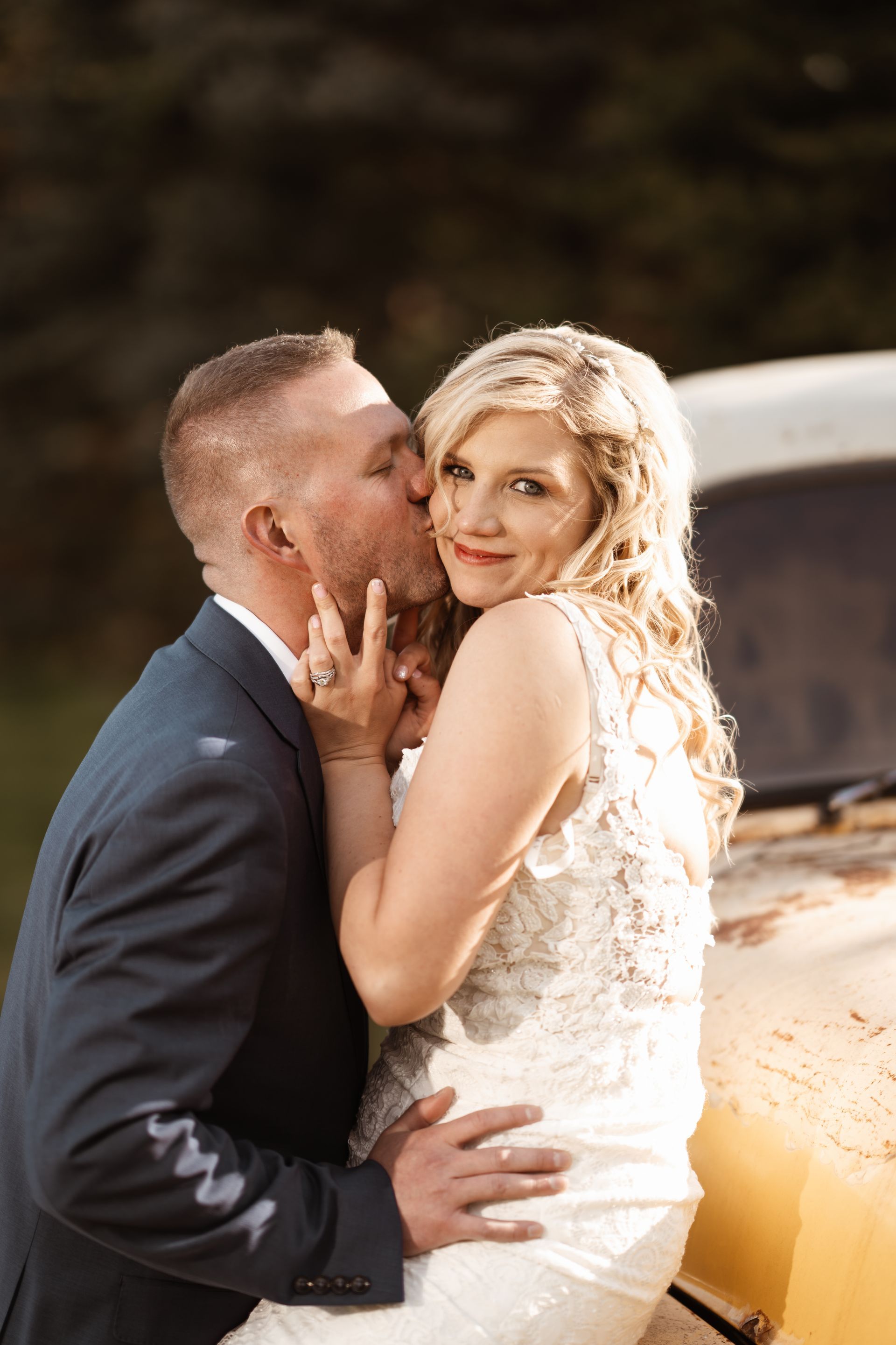 Man kissing bride's cheek; couple poses by yellow vintage truck.