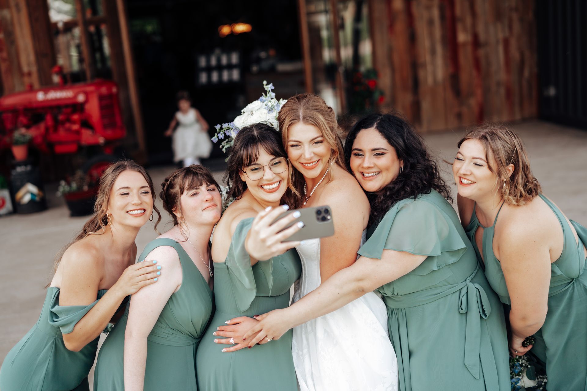 Bride takes a selfie with bridesmaids in green dresses outside a wooden building.