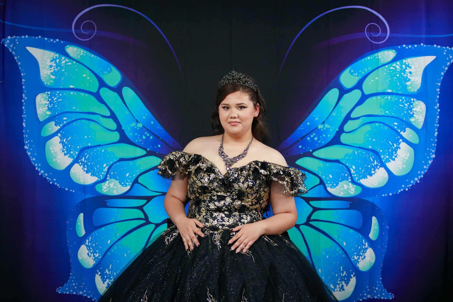 Young person in a sparkly black dress with a butterfly wing backdrop.