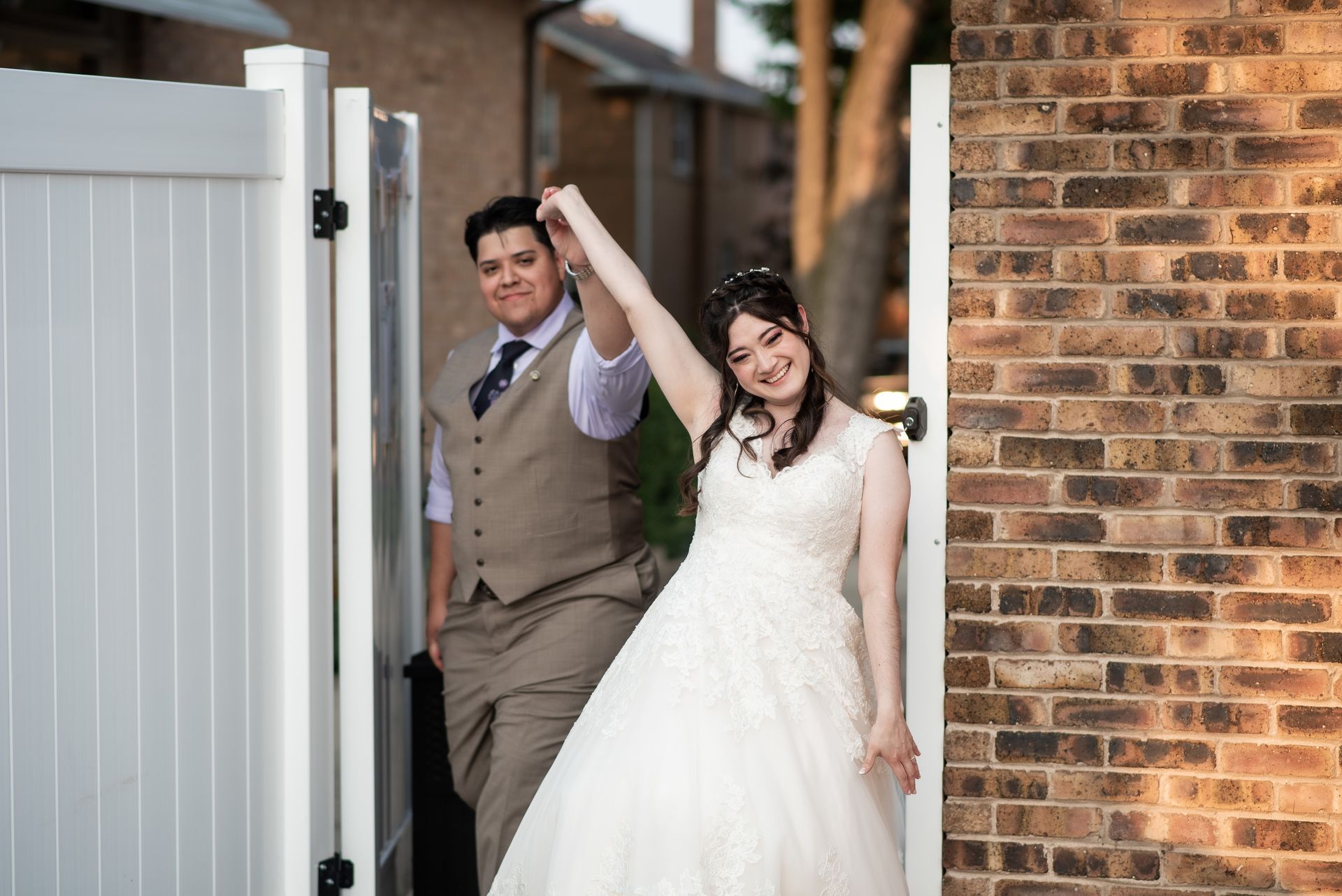 Two people, one in a wedding dress and one in a suit, exiting a gate, arm raised.