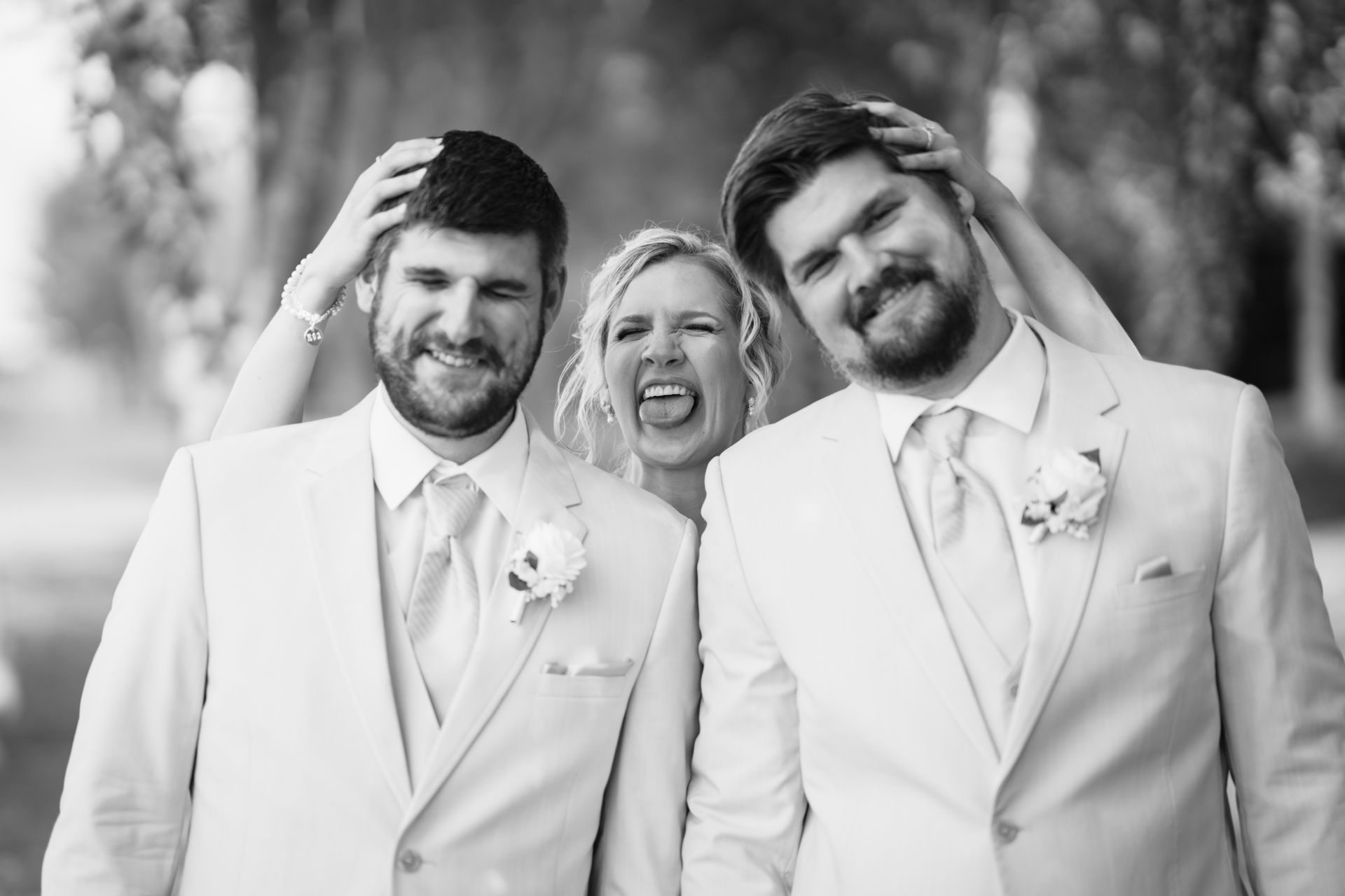 Two men in suits, smiling with hands on their heads; woman making a face between them.