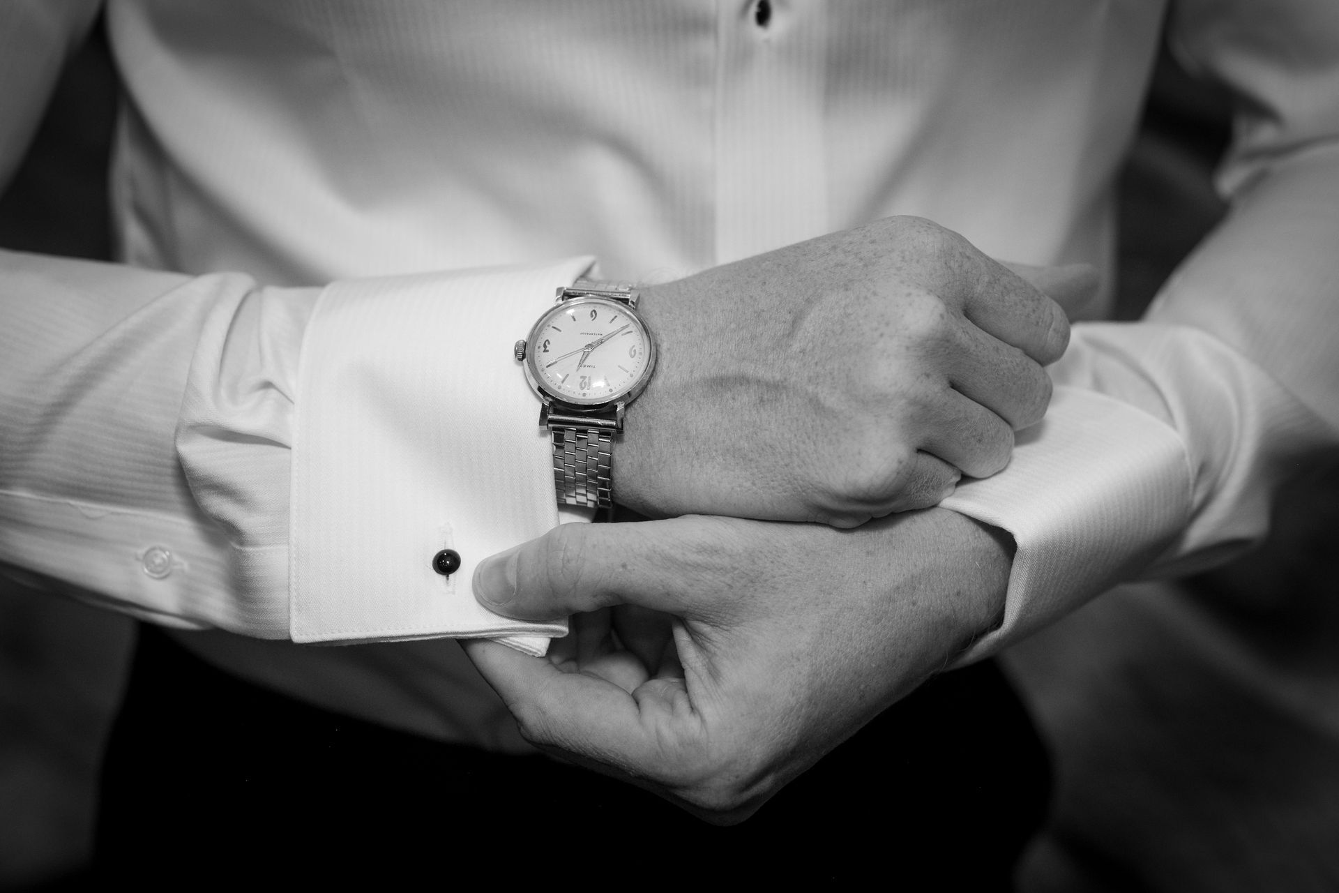 Man in white shirt, silver watch, and cufflink, adjusting his cuff.