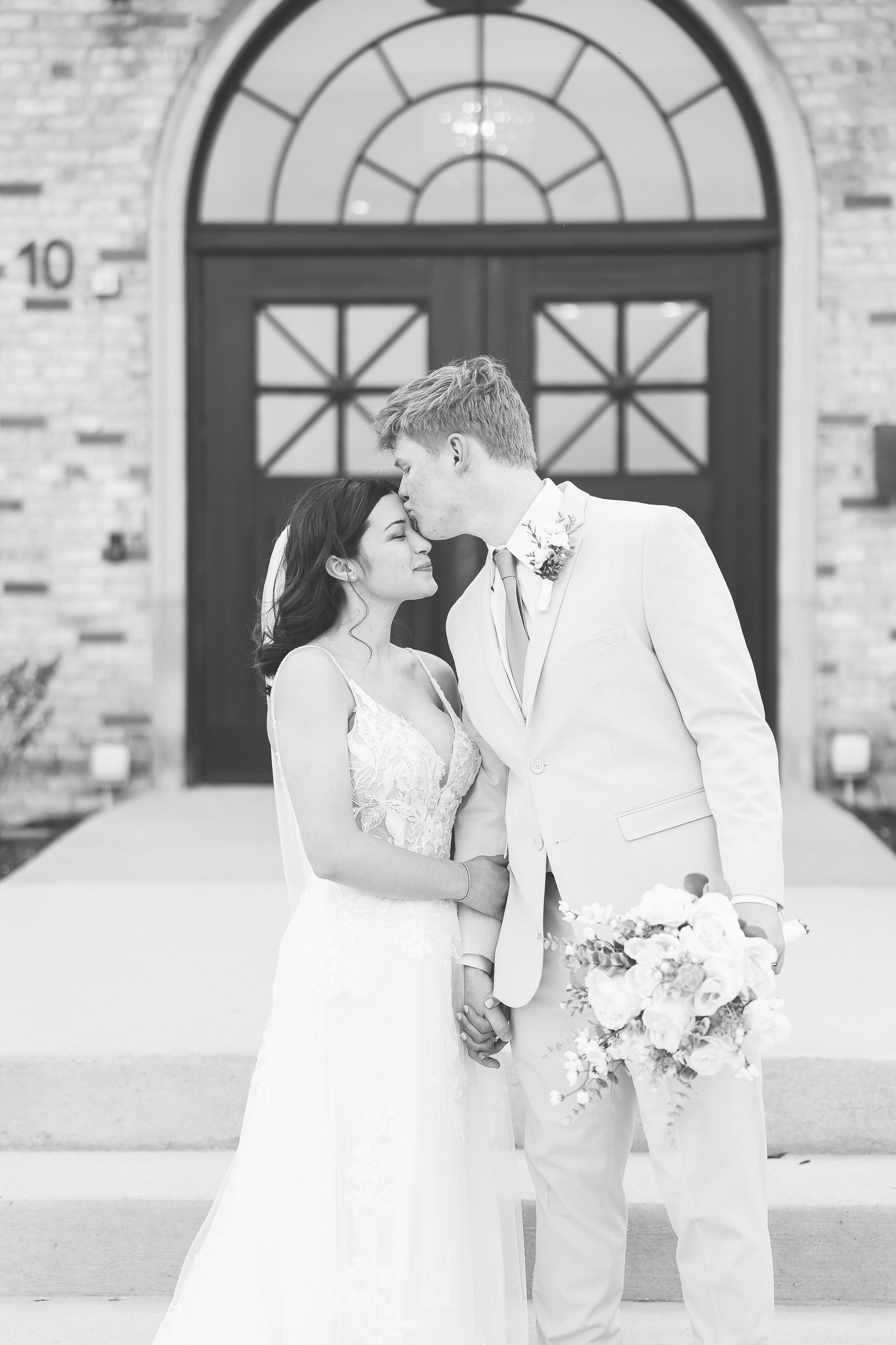 Bride and groom kiss on wedding day. Building with arched doorway in background.