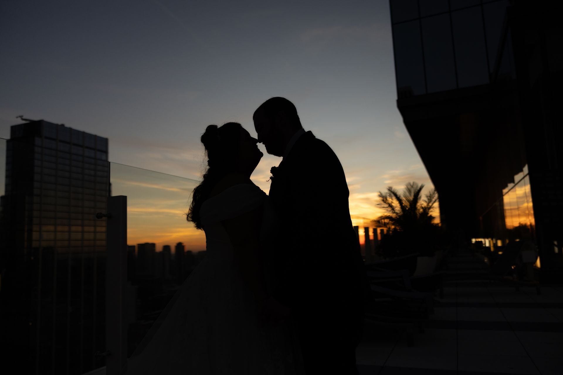 Silhouette of a couple kissing on a rooftop at sunset, with city buildings in the background.