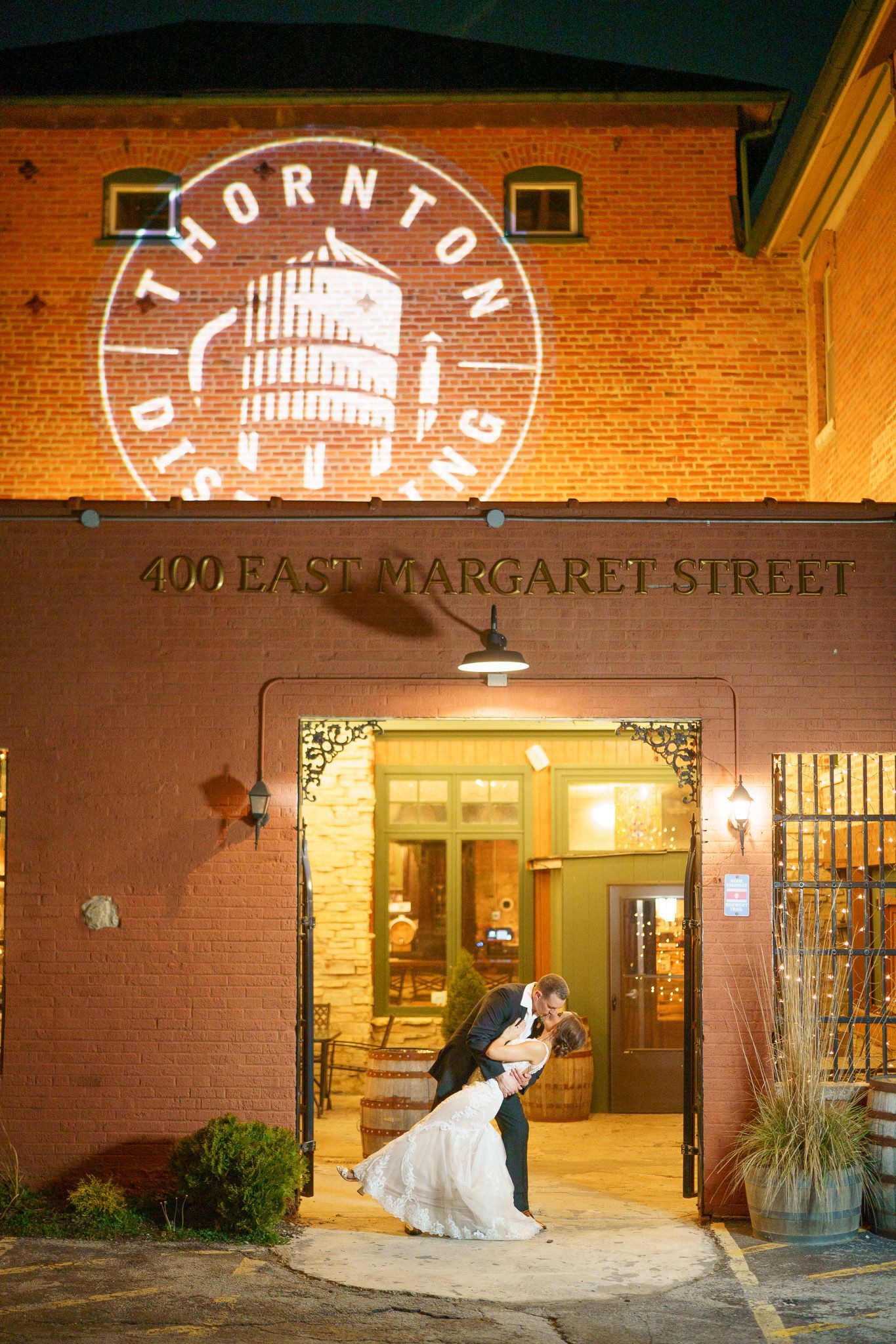 Couple kissing in front of the Thornton Distillery. Building has projection of logo. Night setting.