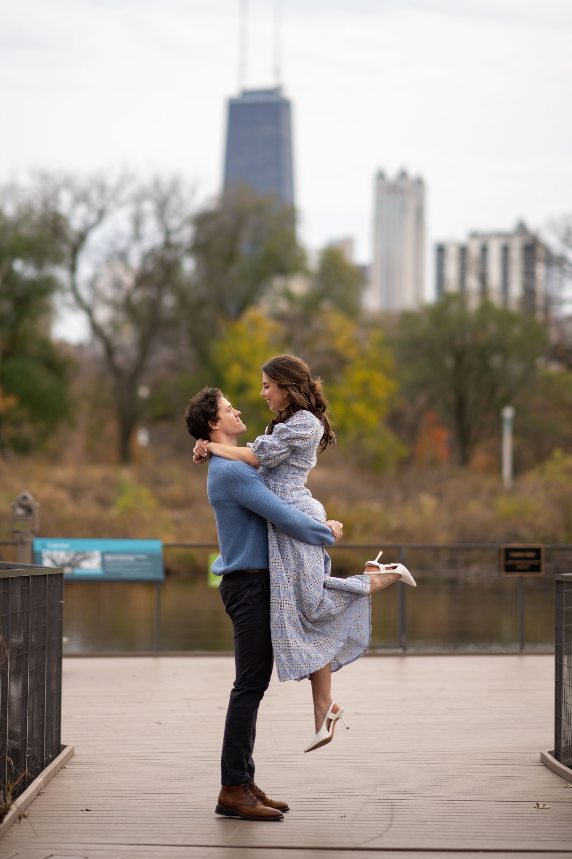 Man lifting woman on a bridge, Chicago skyline in background.