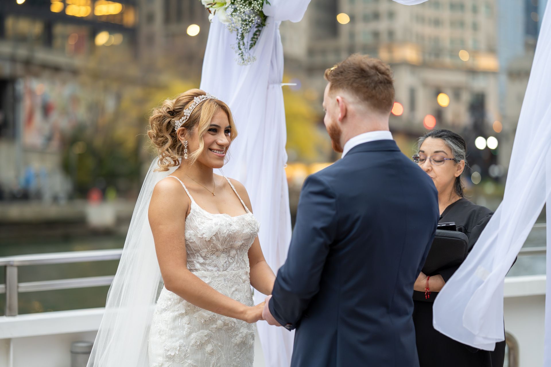 Bride and groom at outdoor wedding ceremony. Bride in white gown, groom in navy suit, smiling.
