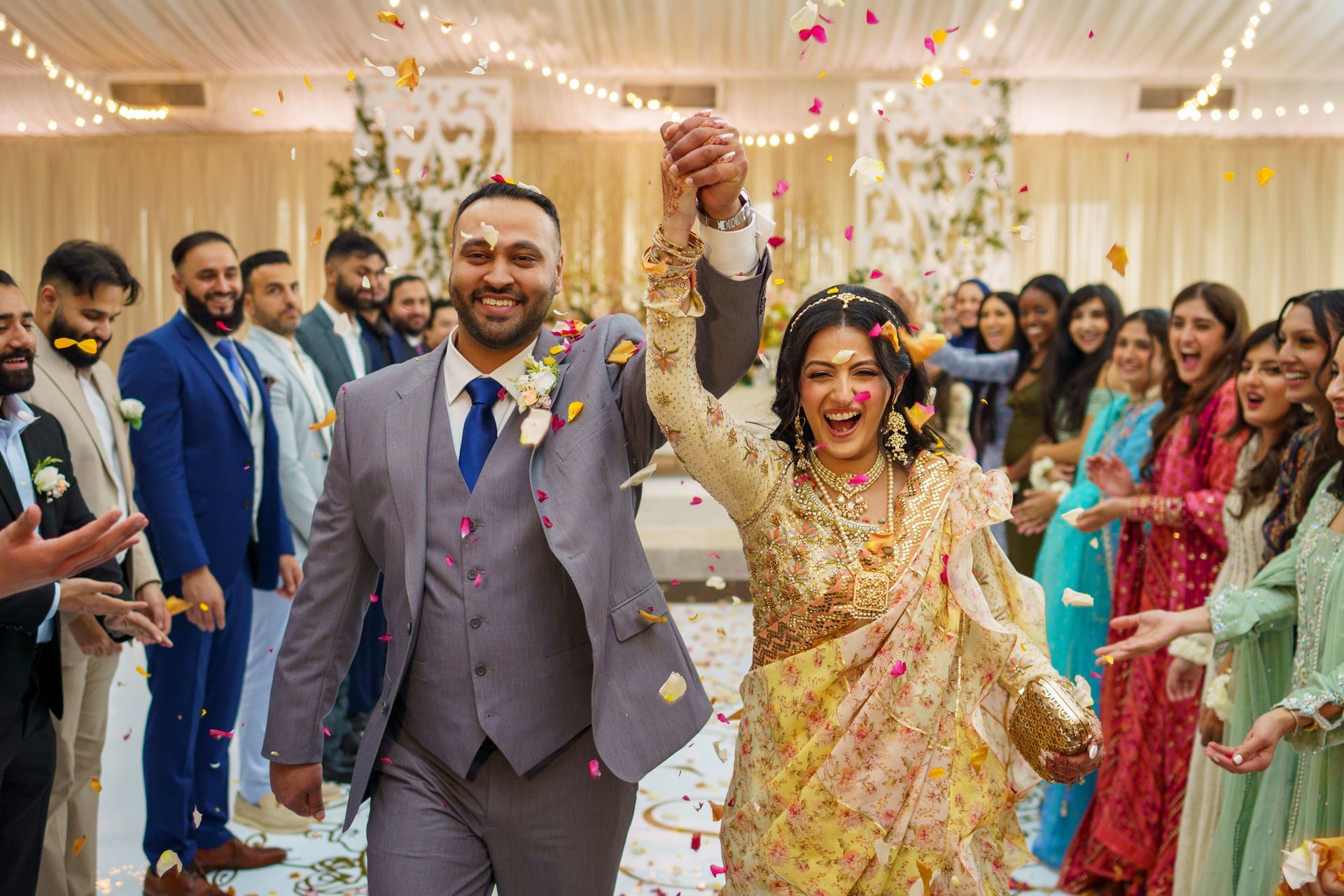 Newly married couple celebrating with flower petals, surrounded by joyful guests.