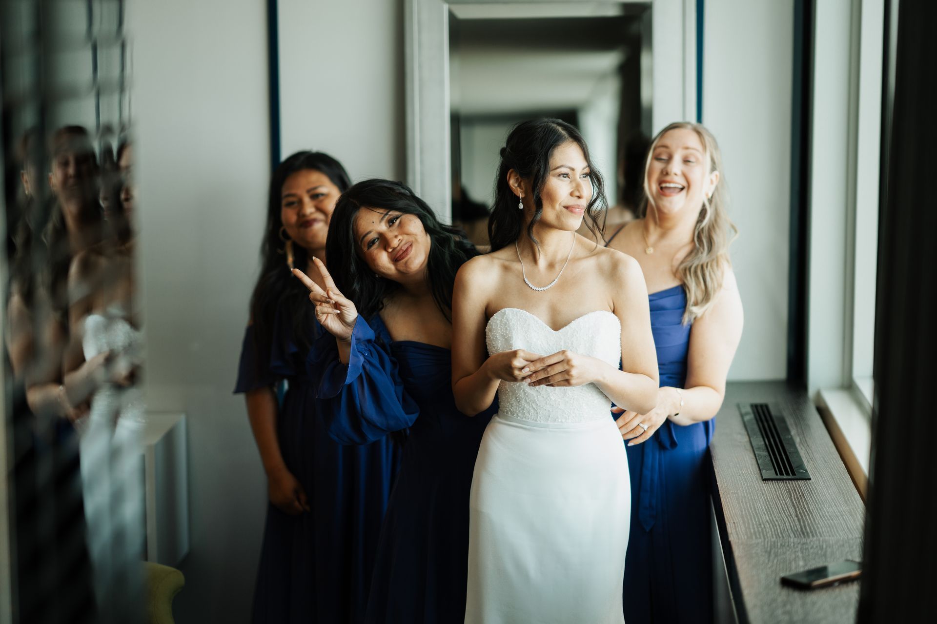 Bride in white dress with bridesmaids in blue dresses, by a window.