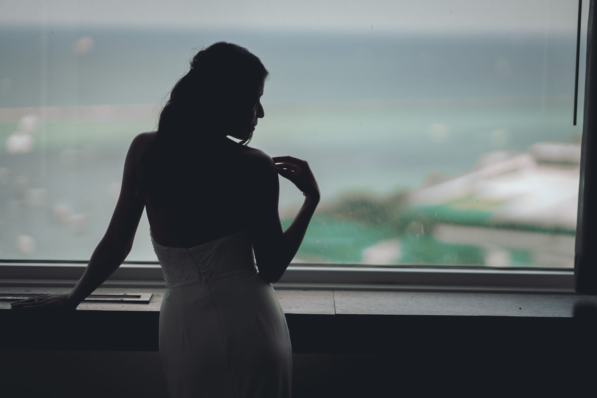 Silhouette of a woman in a dress looking out a window at an ocean view.