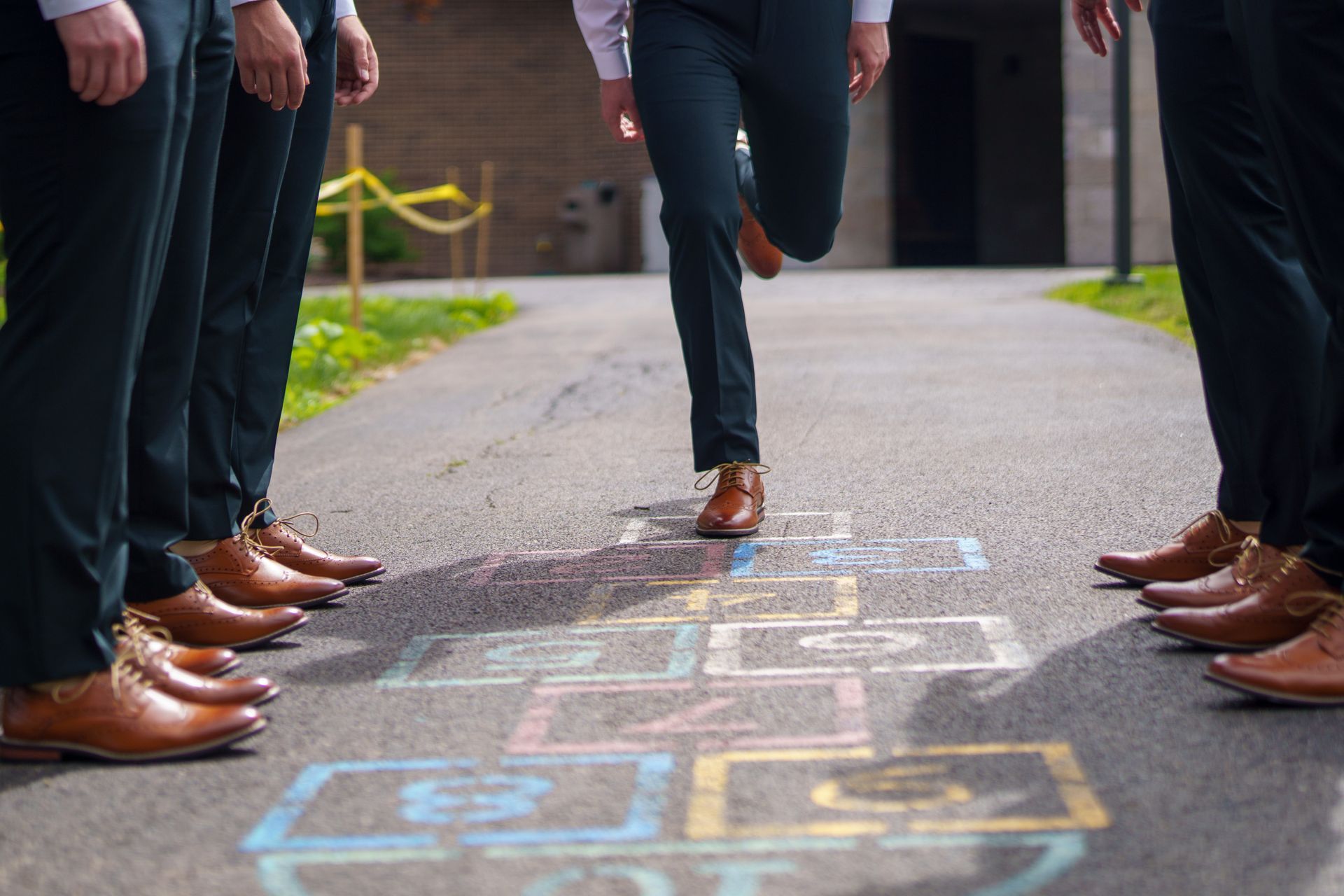 Men in suits playing hopscotch on a sidewalk; one man hops.