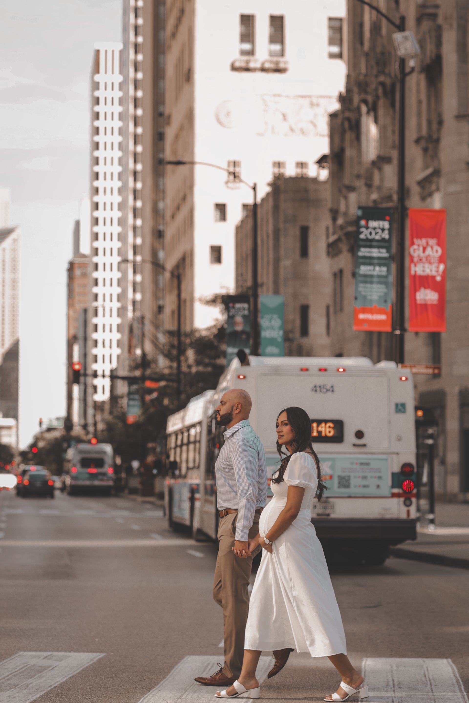 Couple holding hands, crossing street in Chicago. Pregnant woman in white dress, man in button-down.