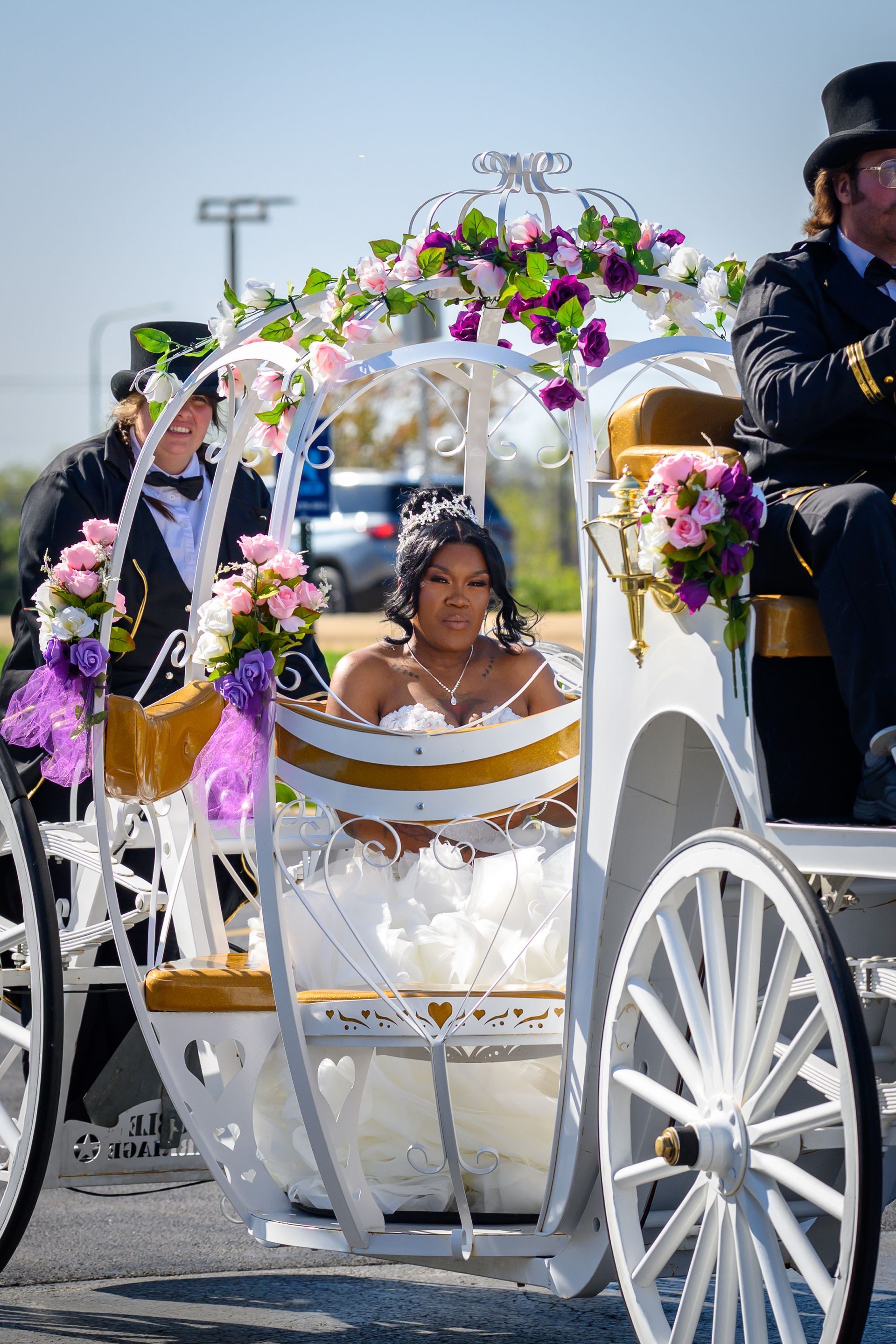 Bride in a white horse-drawn carriage adorned with flowers, smiling. Two men in top hats are visible.