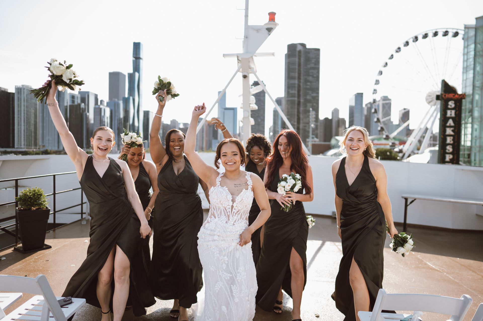 Bridesmaids and bride celebrate on a boat deck with a city skyline and Ferris wheel.