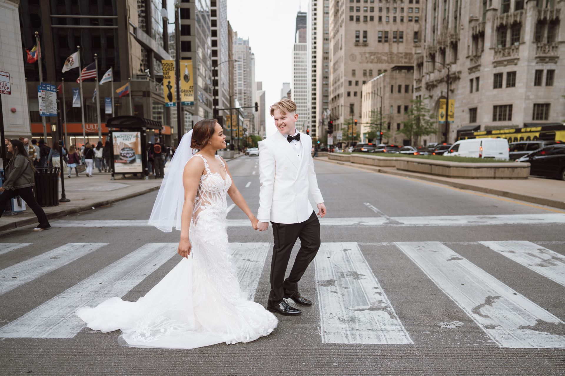 Couple in wedding attire holding hands, crossing a city street.