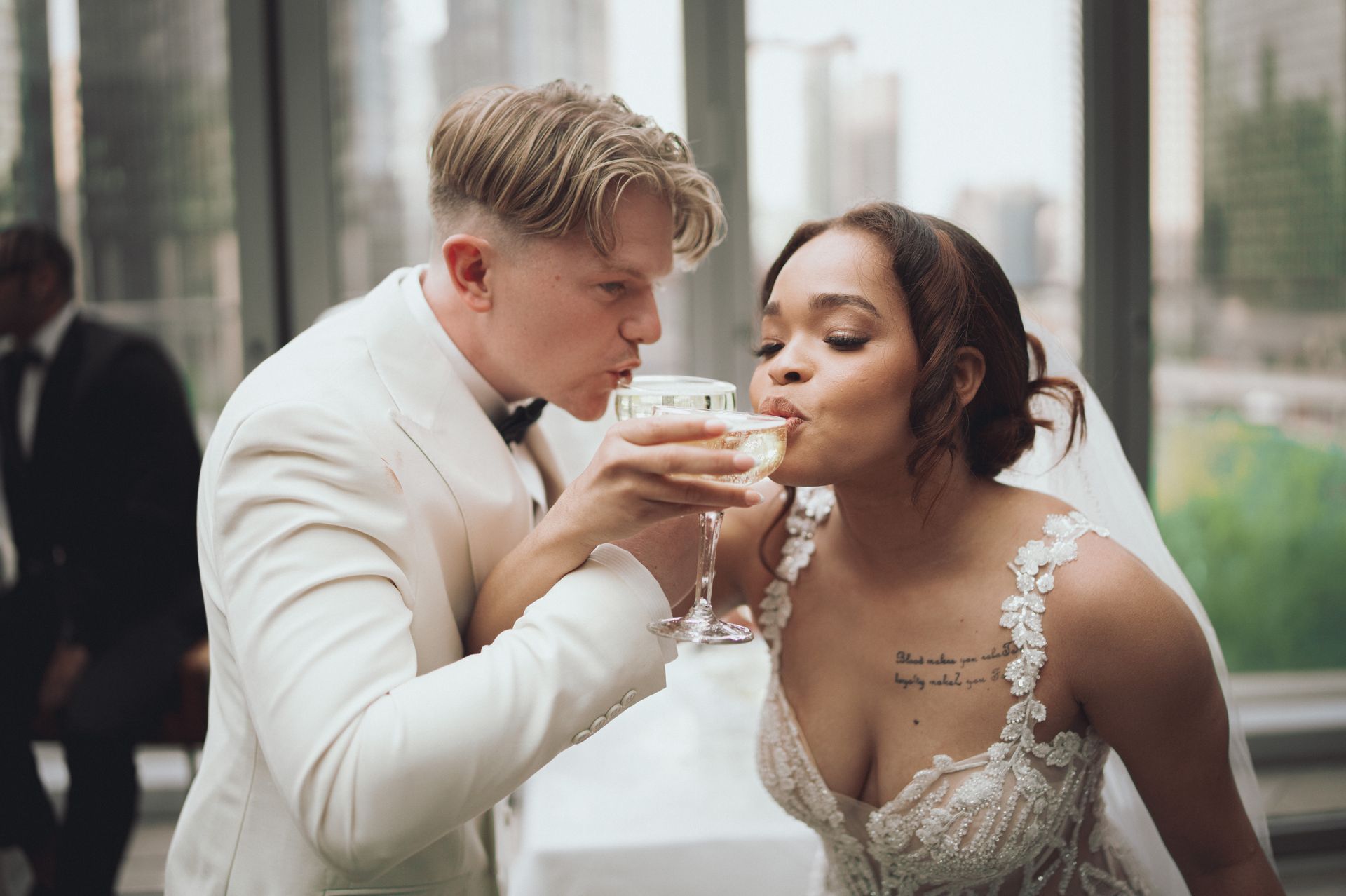 Couple toasting with champagne glasses at a wedding. The groom in a cream suit, the bride in a white gown.