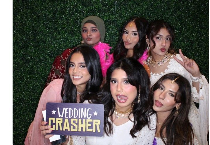 Six people posing in front of a green backdrop, holding a