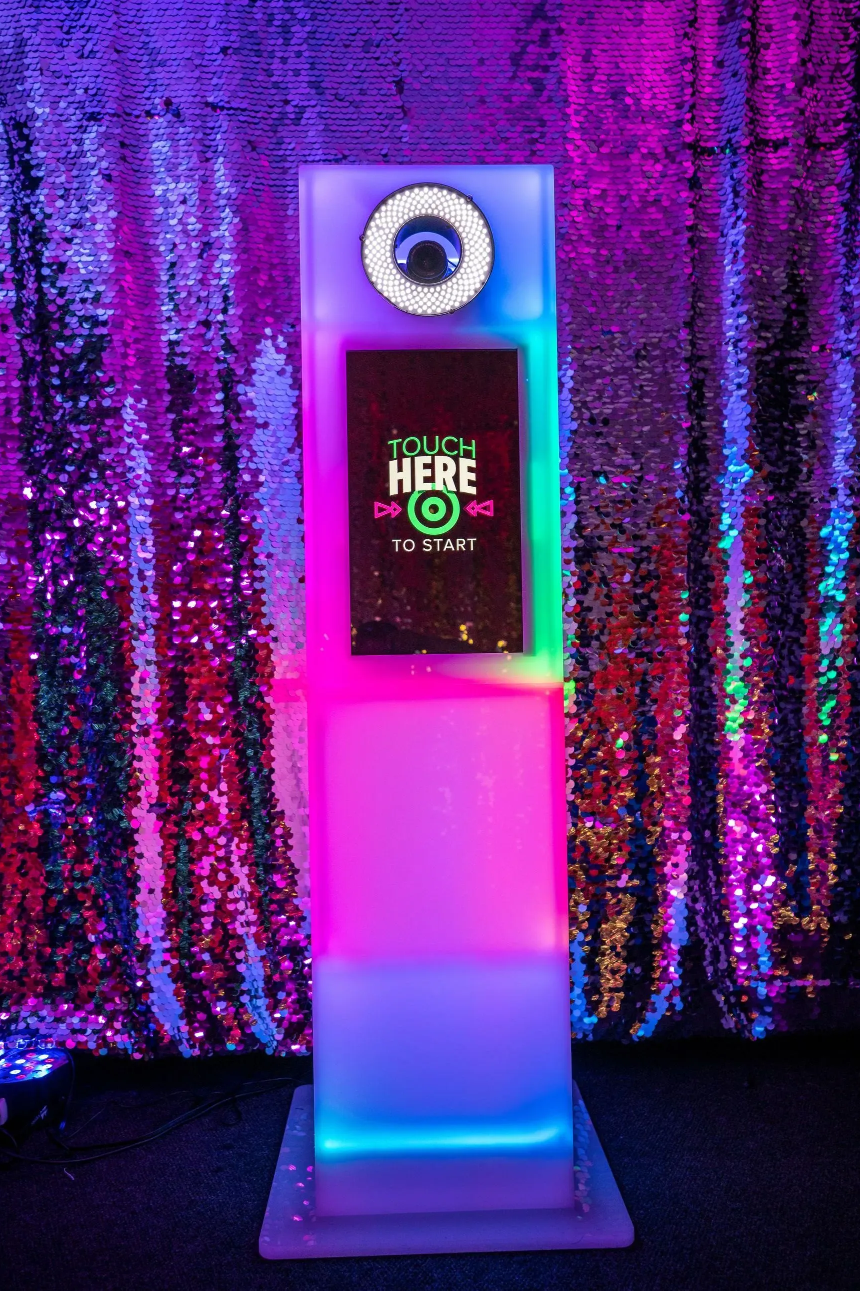 Photo booth with a colorful light display against a sequined backdrop. The screen reads 