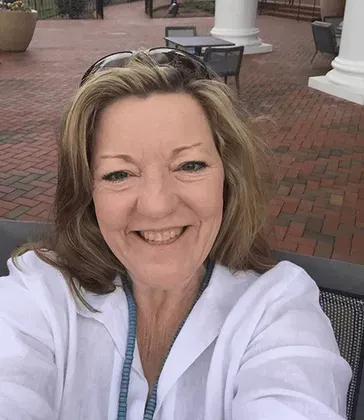 Smiling woman taking a selfie outdoors on a brick patio with white columns in the background