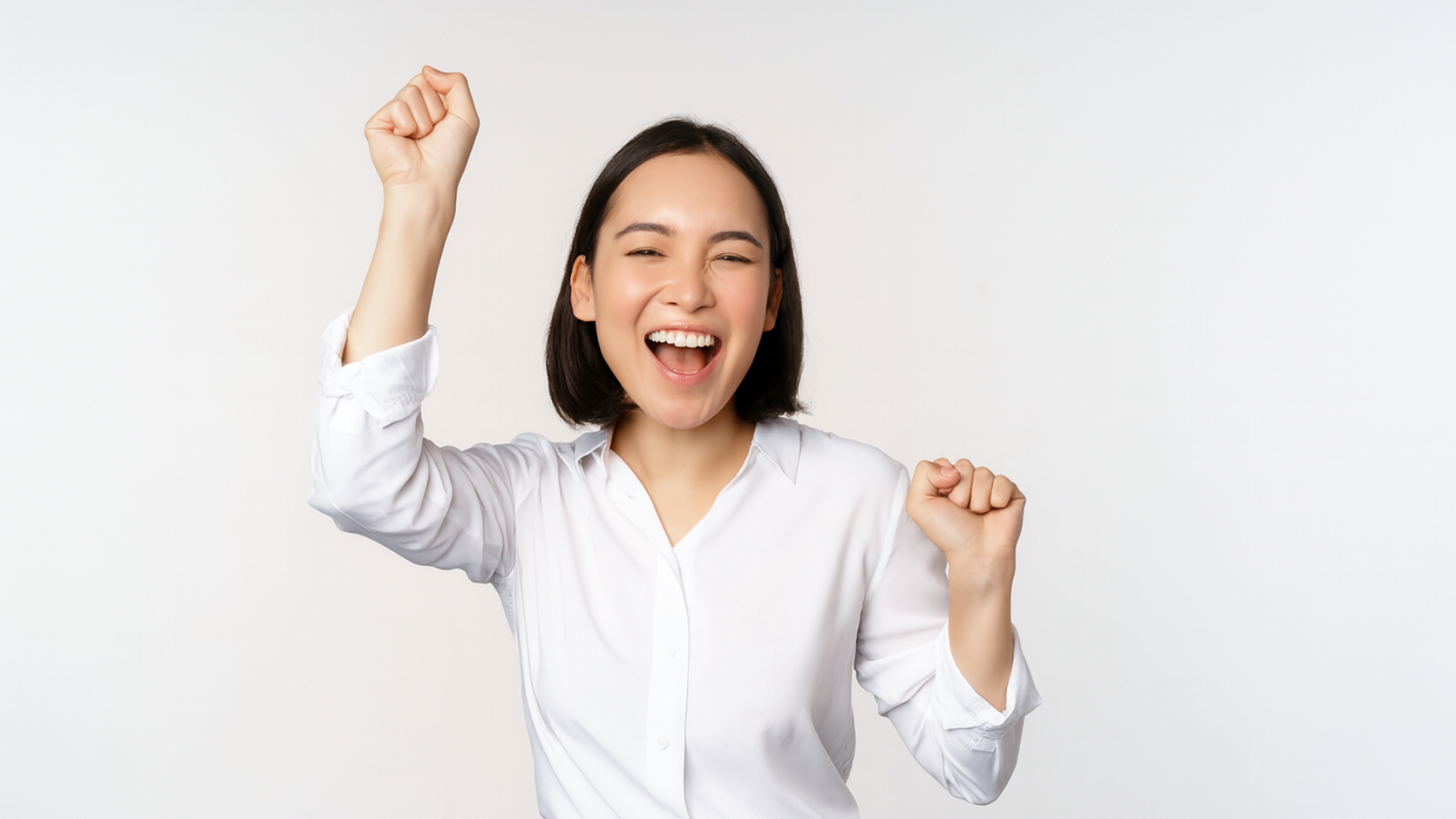 Woman with short dark hair, white shirt, denim jeans, arms raised in excited celebration, open mouth.