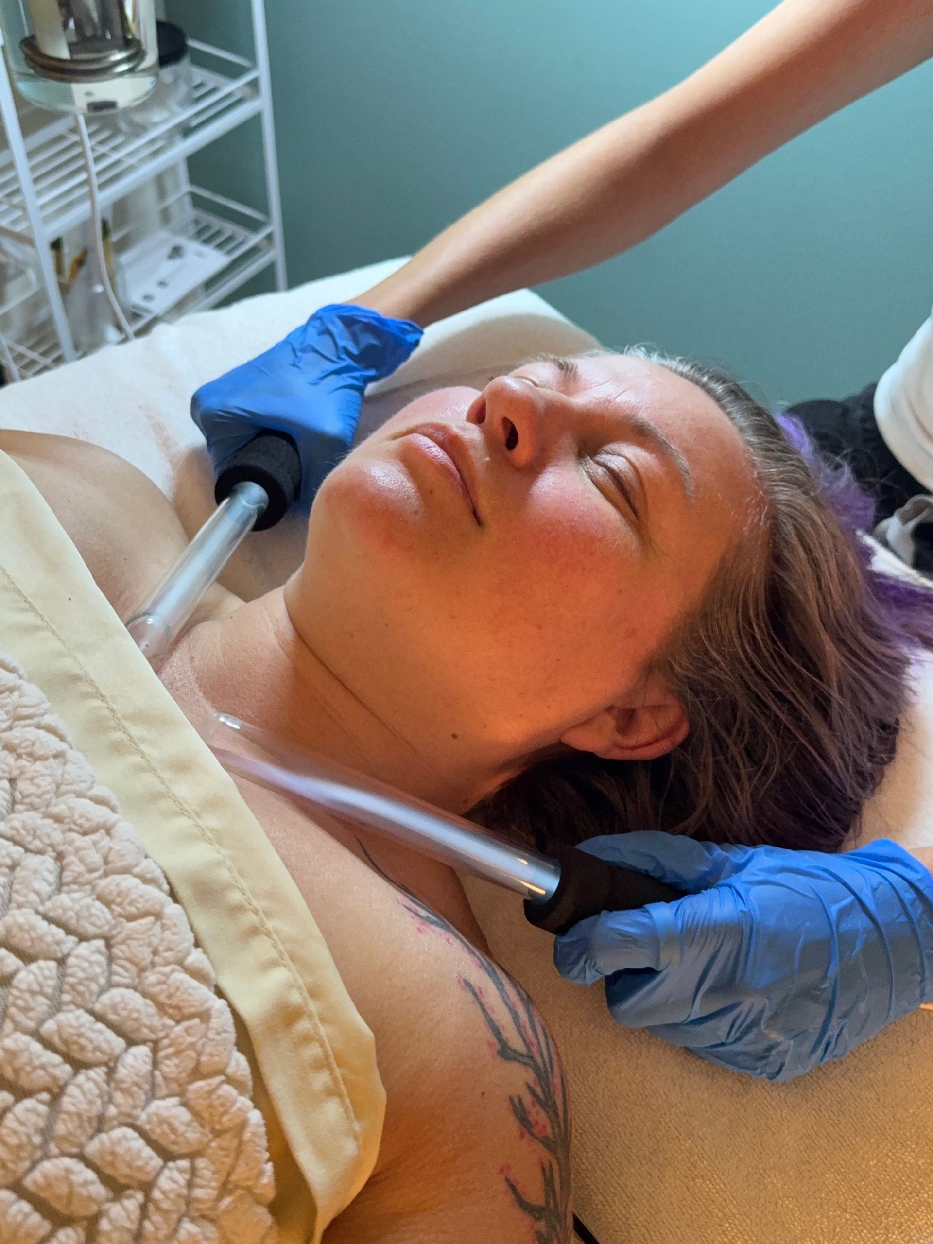 Person receiving a facial treatment while gloved hands adjust equipment near the face.