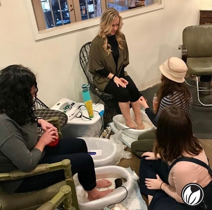 People receiving pedicures in a salon, with foot tubs and a technician working on one client's feet