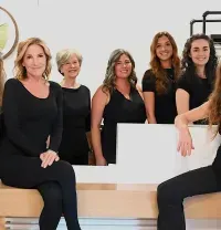 Group of six people seated and standing in a bright salon, smiling at the camera.