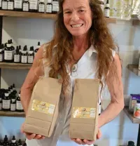 Woman smiling and holding two brown paper bags in a shop with shelves of bottles behind her