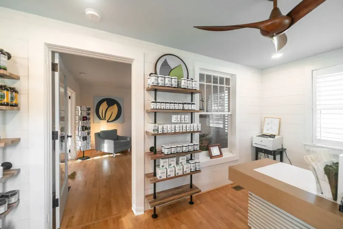 Bright spa room with shelves of products, wooden floor, massage table, and ceiling fan.