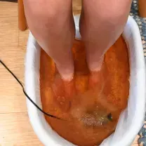 Feet soaking in an orange foot bath in a white basin