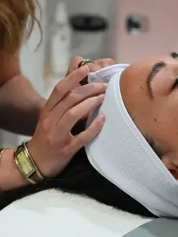 Person receiving a facial treatment while lying on a spa table with a white headband
